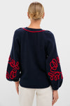 Woman from behind wearing the Navy & Red Soutache Stella Cardigan, featuring balloon sleeves with red embellishments, styled with a low bun and light pants, exuding classic, effortless elegance.