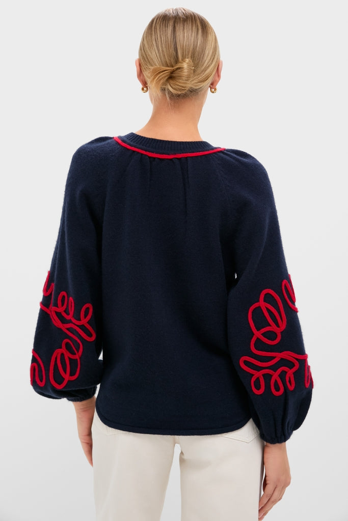Woman from behind wearing the Navy & Red Soutache Stella Cardigan, featuring balloon sleeves with red embellishments, styled with a low bun and light pants, exuding classic, effortless elegance.