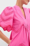 Person wearing a classic, high-end Hot Pink with Red Embroidery Weston Mini Dress featuring effortless puffed sleeves, scalloped embroidery, and a fun V-neckline, with a hand in a side pocket.