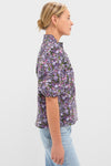 Model wearing the Shades of Purple Floral Florence Blouse, featuring a high ruffled collar and dense floral print, paired with light-wash jeans for a classic, effortless look.
