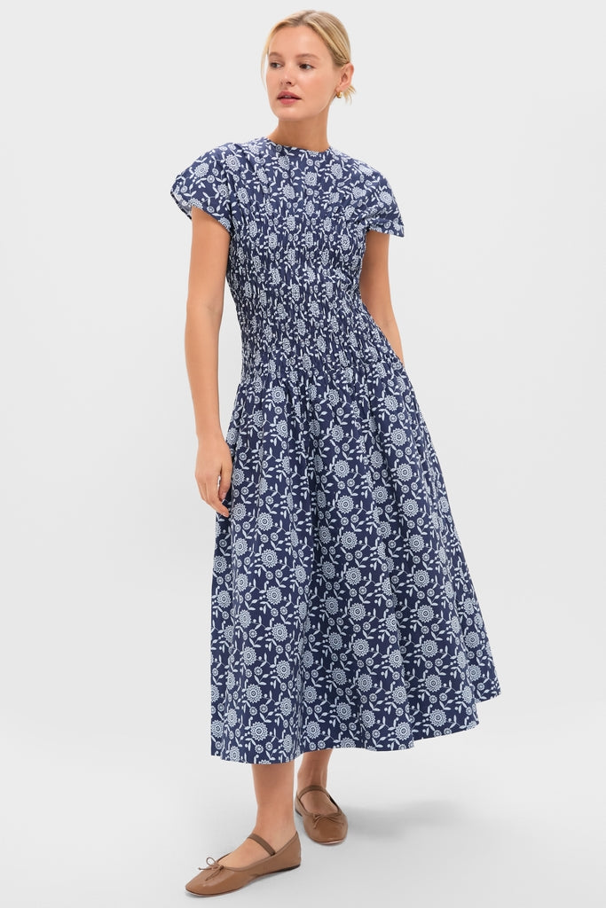 Young woman in Blue Floral Smocked Rollins Midi Dress with flutter sleeves and fitted bodice, embodying classic, effortless style, paired with ballet flats for a fun, high-end look.