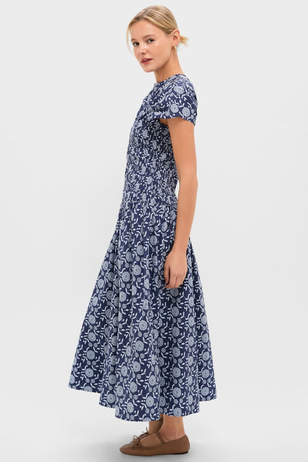 Model in profile wearing the Blue Floral Smocked Rollins Midi Dress, featuring a classic navy-blue floral design, round neckline, and flowing skirt, paired with effortless brown flats.