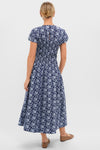 Back view of a woman in the Blue Floral Smocked Rollins Midi Dress featuring classic white floral prints, effortless puffed sleeves, and a fun, high-end smocked waist.