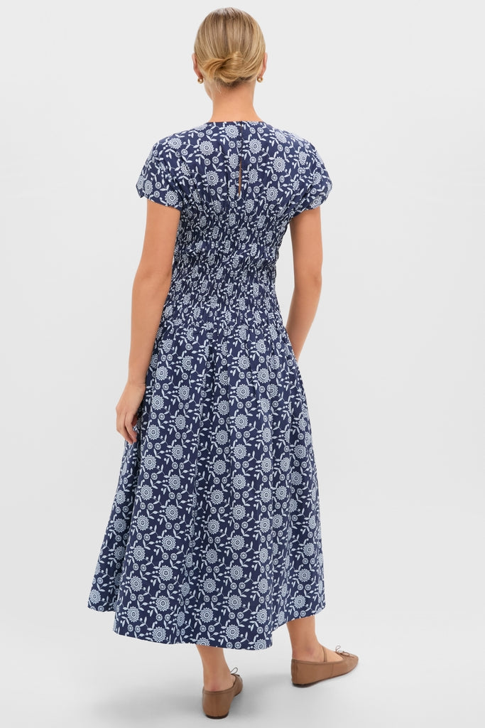 Back view of a woman in the Blue Floral Smocked Rollins Midi Dress featuring classic white floral prints, effortless puffed sleeves, and a fun, high-end smocked waist.