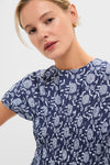Young woman models the Blue Floral Smocked Rollins Midi Dress, featuring a classic, high-end navy-blue blouse with effortless white floral print and fun smocked waist.