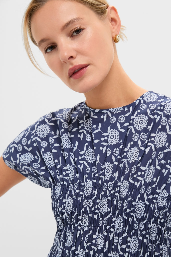 Young woman models the Blue Floral Smocked Rollins Midi Dress, featuring a classic, high-end navy-blue blouse with effortless white floral print and fun smocked waist.