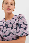 Woman in a classic, high-end Pink & Navy Floral Jacquard Minetta Mini Dress, exuding effortless elegance with fun floral patterns, complemented by small gold hoop earrings.