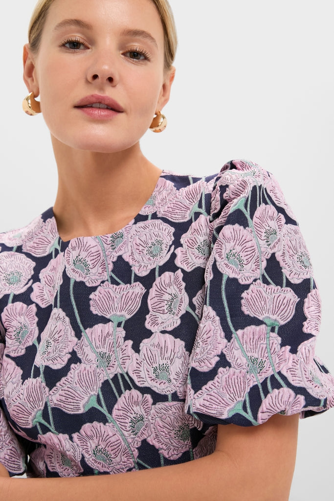 Woman in a classic, high-end Pink & Navy Floral Jacquard Minetta Mini Dress, exuding effortless elegance with fun floral patterns, complemented by small gold hoop earrings.