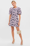 Model in Pink & Navy Floral Jacquard Minetta Mini Dress, showcasing its classic, effortless style with puffed sleeves and a high-end finish, paired with a fun clutch and platform sandals.
