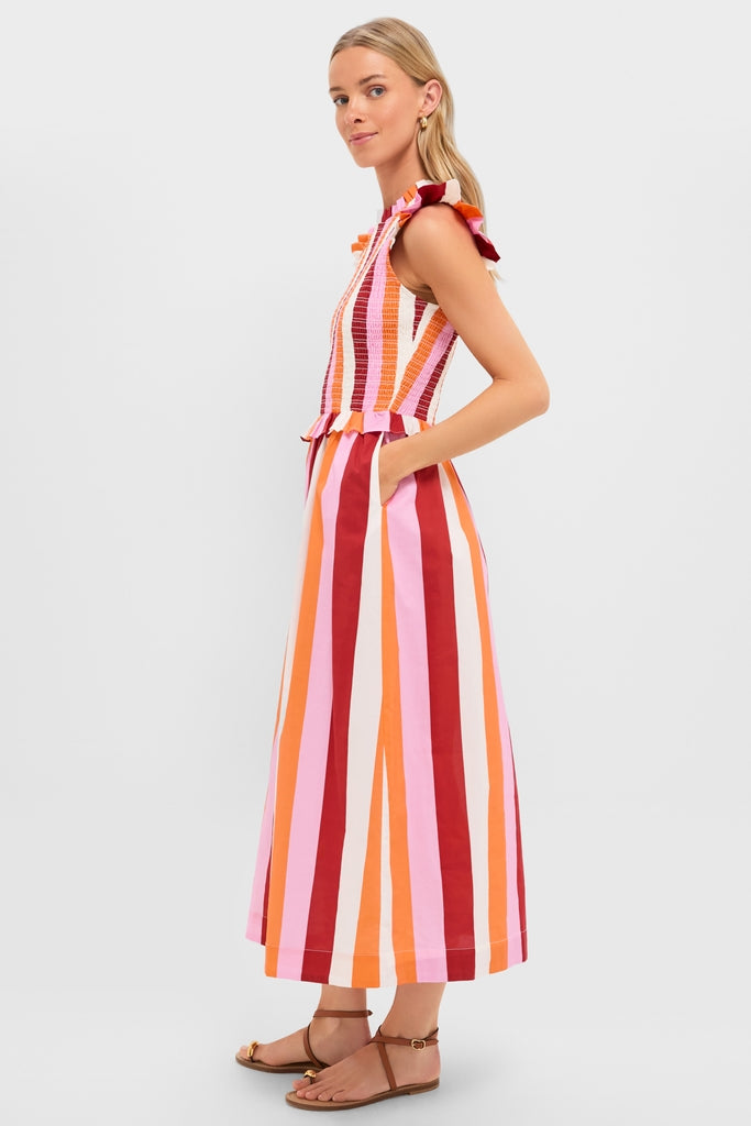 Model in profile wearing the classic, effortless Orange, Pink & Crimson Stripe Smocked Sully Dress, featuring fun ruffled details, with high-end gold hoop earrings and brown leather sandals.