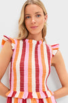 Young woman wears classic, high-end Orange, Pink & Crimson Stripe Smocked Sully Dress with ruffle trim, showcasing an effortless and fun look against a light background.