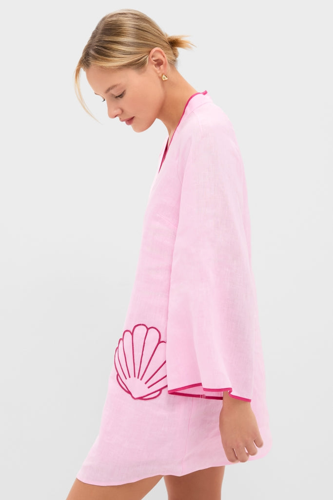 Young woman in profile wearing the Pink Seashell Oceana Mini Dress, a classic, effortless linen-like tunic with a hood, wide sleeves, and scallop-shell embroidery.