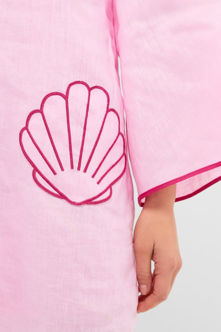 Pink Seashell Oceana Mini Dress, a classic and effortless pale pink linen garment with dark pink embroidered seashells, wide sleeves, and a child's hand showcasing its high-end, fun design.