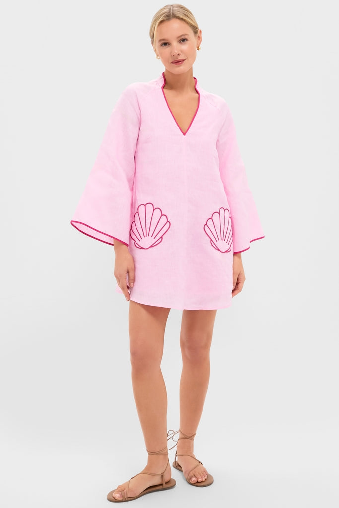 Woman models the classic Pink Seashell Oceana Mini Dress in pale pink linen with effortless bell sleeves, fun fuchsia-trimmed V-neck, and high-end shell-shaped appliqués.