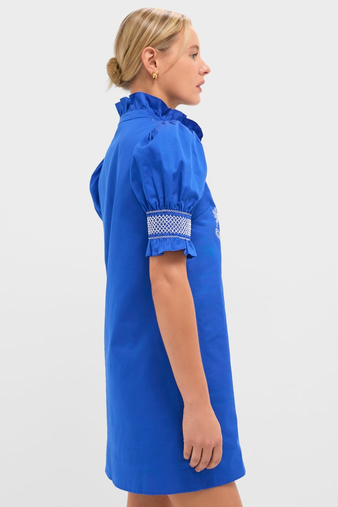 Woman in profile wearing the Royal Blue with White Embroidery Lou Lou Mini Dress, featuring a ruffled neckline, puffed sleeves, and smocked embroidery, exuding a classic and effortless high-end style.
