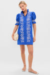Model wearing the Royal Blue with White Embroidery Lou Lou Mini Dress, featuring classic floral embroidery, a ruffled collar, and puffed sleeves, paired with a cream clutch and white sandals.