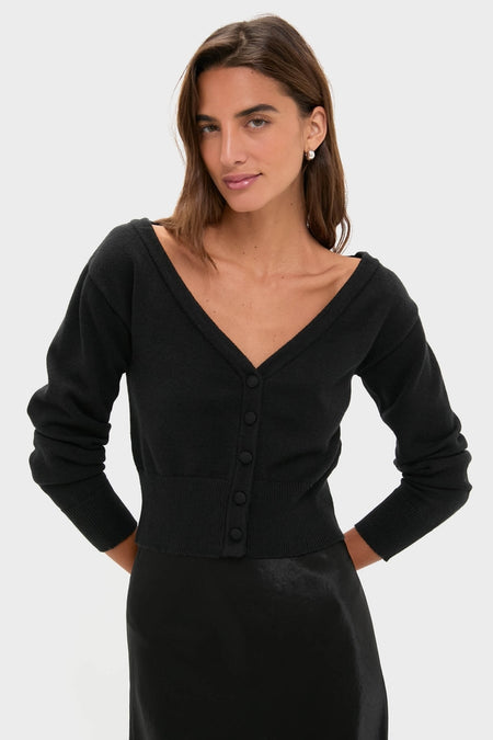 Fashion model showcases the Black Off the Shoulder Stevens Sweater with deep V-neck, fabric-covered buttons, and fitted waist, paired with a silky skirt for an effortless, high-end look.