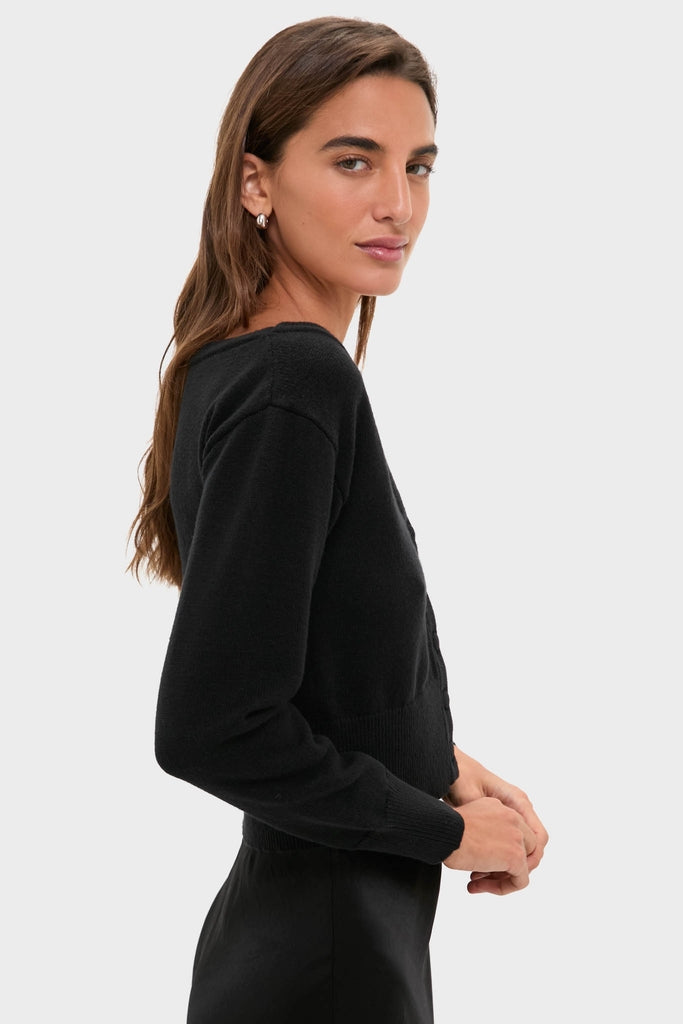 Young woman in profile wearing the Black Off the Shoulder Stevens Sweater, showcasing its deep V-neckline and fitted waist, embodying a classic, effortless, high-end look.