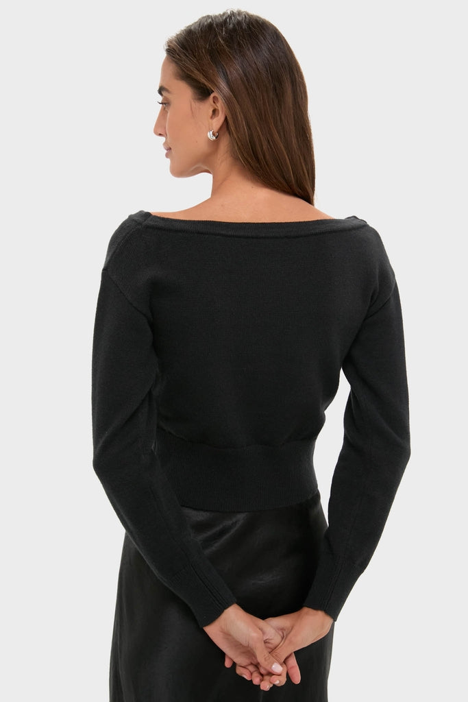 Woman in a classic black off-shoulder Stevens sweater, showcasing an effortlessly high-end style with a deep V-neckline and fitted waist, embodying fun and confidence.