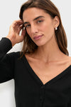 Young woman in Black Off the Shoulder Stevens Sweater, showcasing a classic, effortless style with a deep V-neck and button closure, embodying high-end, fun fashion.