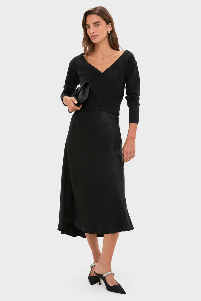 Model in a classic Black Off the Shoulder Stevens Sweater, paired with a satin skirt and slingback heels, showcasing an effortless, high-end, fun look.