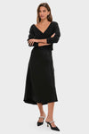 Black Off the Shoulder Stevens Sweater with deep V-neck and button closure, styled effortlessly with a bias-cut skirt and heels for a classic, high-end look.