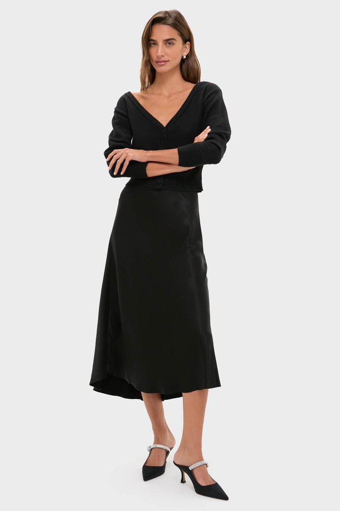 Black Off the Shoulder Stevens Sweater with deep V-neck and button closure, styled effortlessly with a bias-cut skirt and heels for a classic, high-end look.