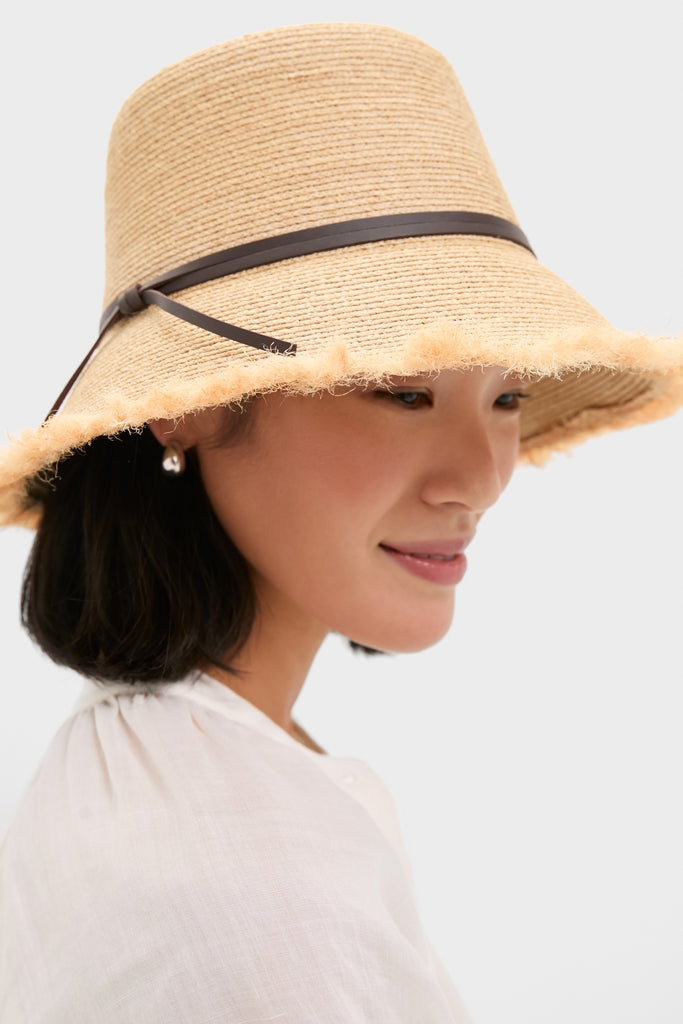 Woman wearing the classic Natural and Chocolate Zoe Lampshade Hat, showcasing its wide-brim design and slim dark band, paired effortlessly with a light white blouse.