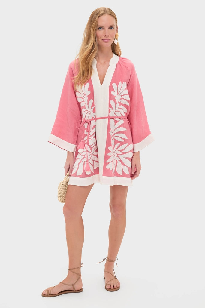 Model wearing the Flora Pink Lumi Mini Dress, a classic kimono-style tunic with bold white leaf embroidery, exuding effortless elegance, paired with a woven clutch and strappy sandals.