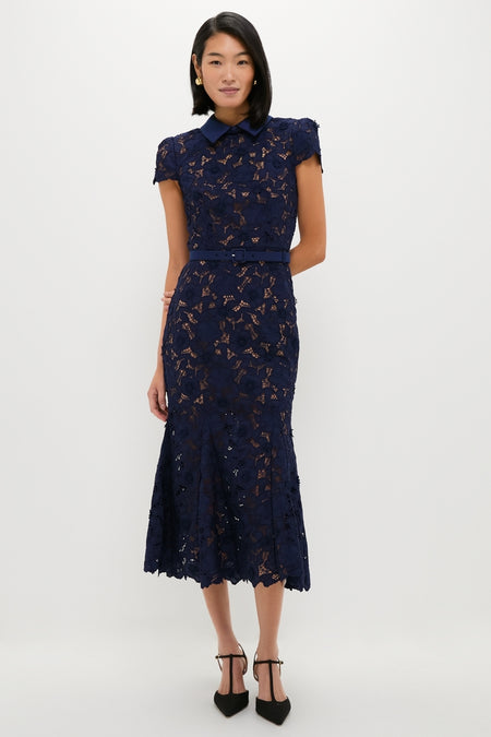 Navy Guipure Lace Midi Dress on model: classic design with pointed collar, capped sleeves, slim belt, floral lace overlay, and flared hem, paired with black T-strap heels. Effortless and high-end.