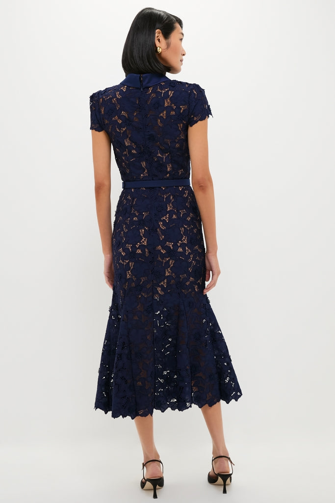 Woman in a Navy Guipure Lace Midi Dress, featuring a classic floral-lace design, fitted waist with belt, and gently flared skirt, paired with strappy heels for an effortless, high-end look.