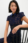 Young woman in a classic, effortless Navy Guipure Lace Midi Dress sits on a chair, showcasing its high-end floral embroidery and fun, pointed collar design.