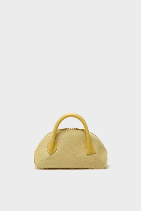 Butter EW Dome Clutch: A classic, dome-shaped handbag in muted yellow with short handles, zip closure, and a textured finish, exuding an effortless, high-end, fun style.