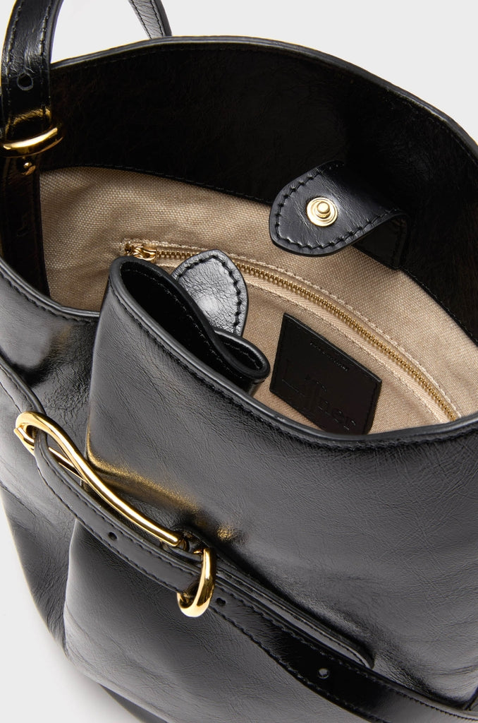 Black Glossy Belted Bucket Bag with a classic and high-end design, featuring an effortless magnetic snap, beige lining, interior zip pocket, and fun adjustable strap.