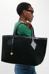 Person carrying a Black Suede Large Sprout Tote with leather-trimmed handles and a gold-tone charm, embodying a classic, effortless, and high-end style.