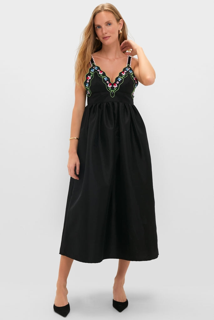 Woman models the Black Selene Dress, a sleeveless midi with a scalloped V-neckline, floral accents, and a classic A-line silhouette, exuding effortless, high-end style.