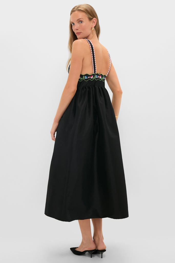 Model in Black Selene Dress with scalloped trim and patterned straps, styled with small hoops and black mules, exuding effortless, classic elegance.