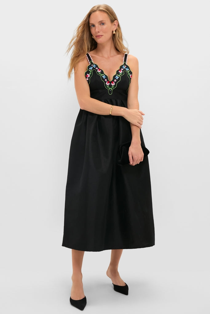 Woman in Black Selene Dress with floral embroidery, holding a clutch. The dress features a classic, effortless style, perfect for a fun, high-end look.