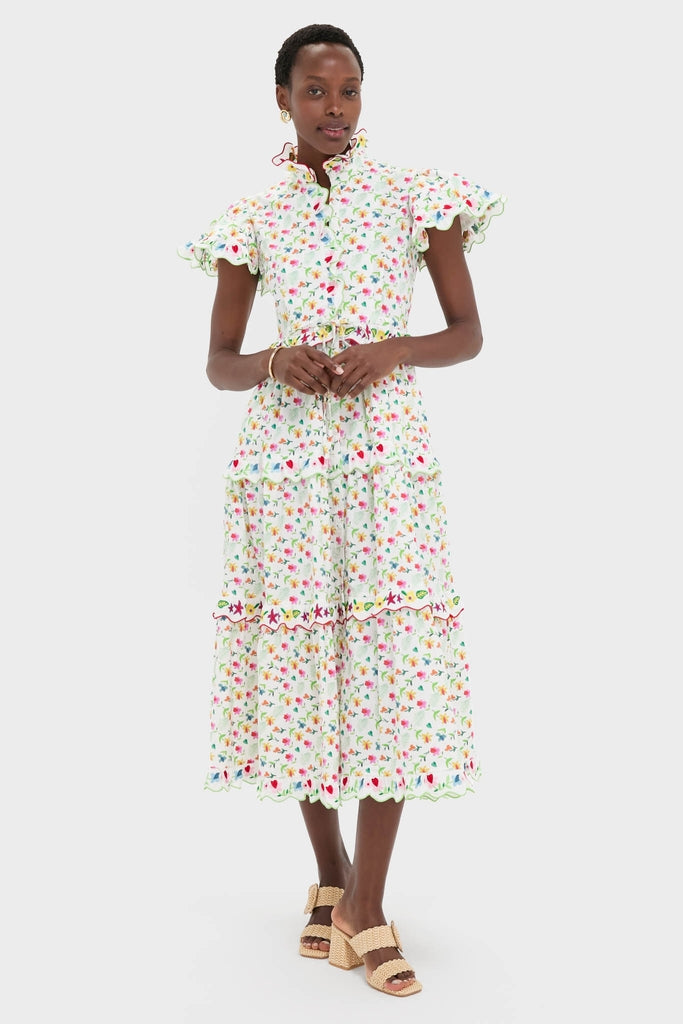 Woman models the classic White Nebula Dress with floral print, high ruffled collar, flutter sleeves, tiered skirt, and effortless drawstring waist, paired with fun block-heel sandals.