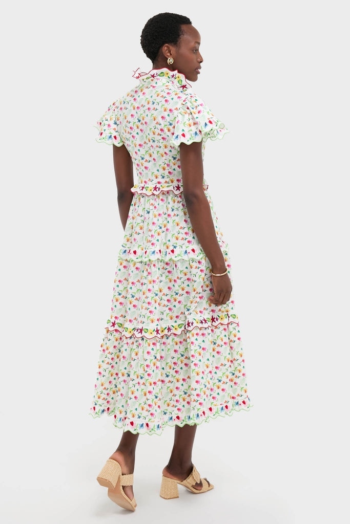 Woman in a classic, effortless White Nebula Dress with ditsy floral print, ruffled collar, and scalloped trims, paired with high-end, fun woven mules.