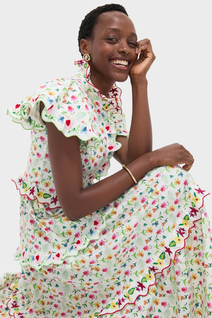 Smiling woman in a classic, high-end White Nebula Dress with vibrant floral print, showcasing effortless style and fun ruffled sleeves, complemented by gold hoop earrings and a bangle.