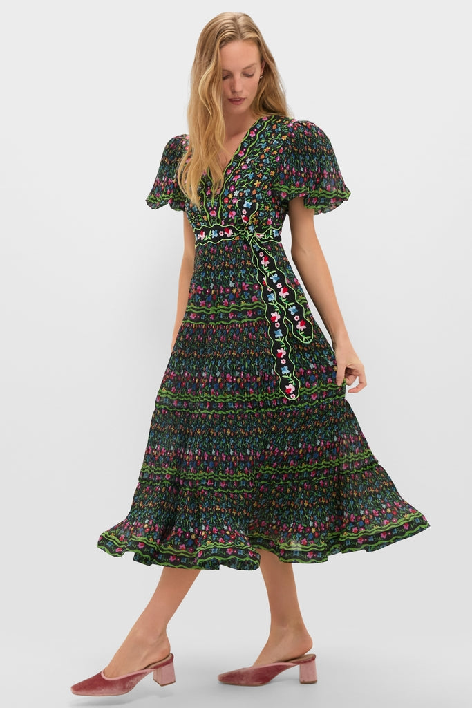 Woman models classic Black Celestia Dress with flutter sleeves, V-neck, and wrap style. Features include floral print, self-tie belt, and ruffled hem for an effortless, high-end look.