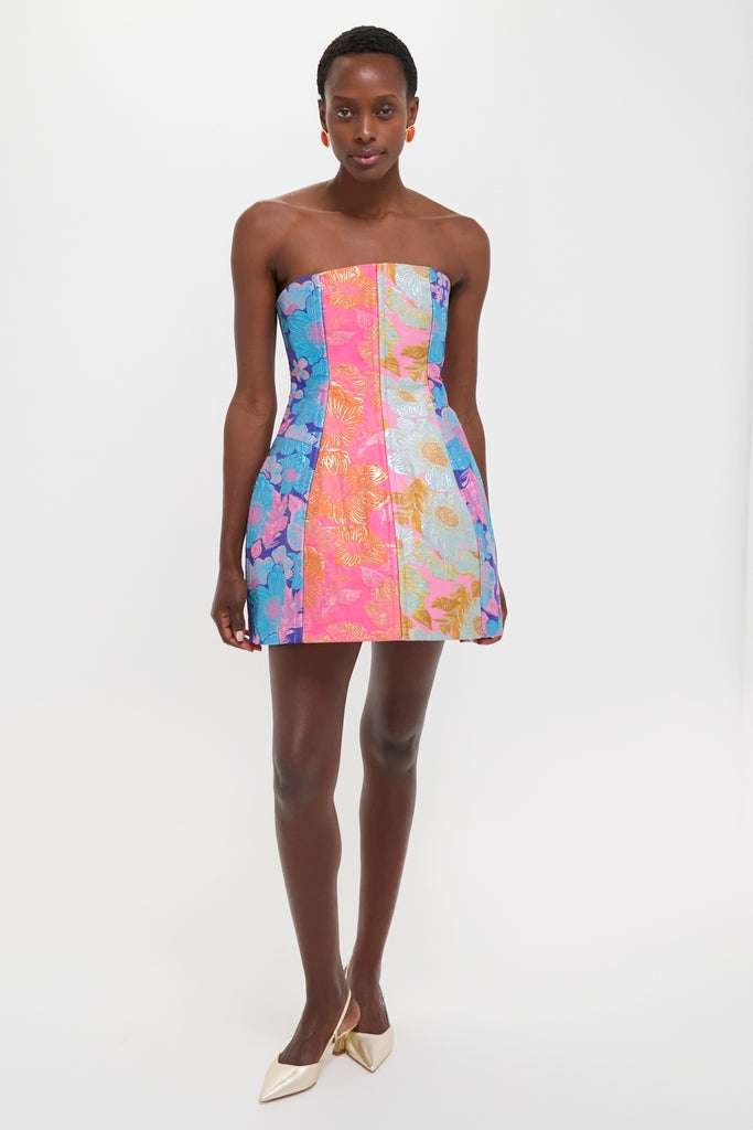Model in Multi Cosmica Dress, a strapless A-line mini with floral brocade panels, paired with metallic slingback heels; exudes classic, effortless, and fun high-end style.