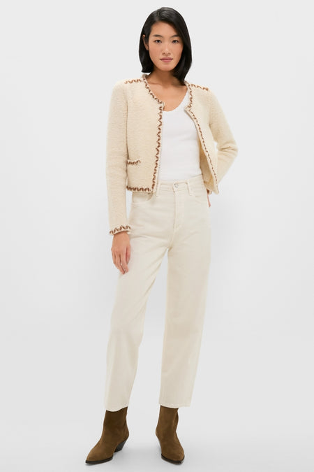 Woman models the classic Ecru and Bronze Rochelle Cardigan with contrasting trim, paired effortlessly with off-white jeans and olive-brown suede boots for a chic, high-end look.