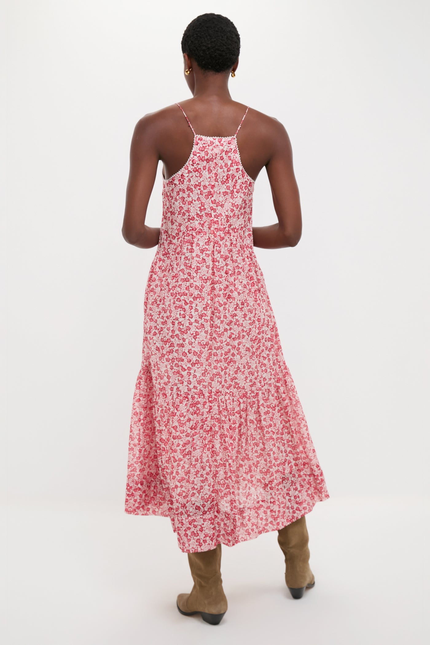 Person in a classic Red Sabba Dress with a tiered silhouette and spaghetti straps, styled effortlessly with suede boots for a fun, high-end look.