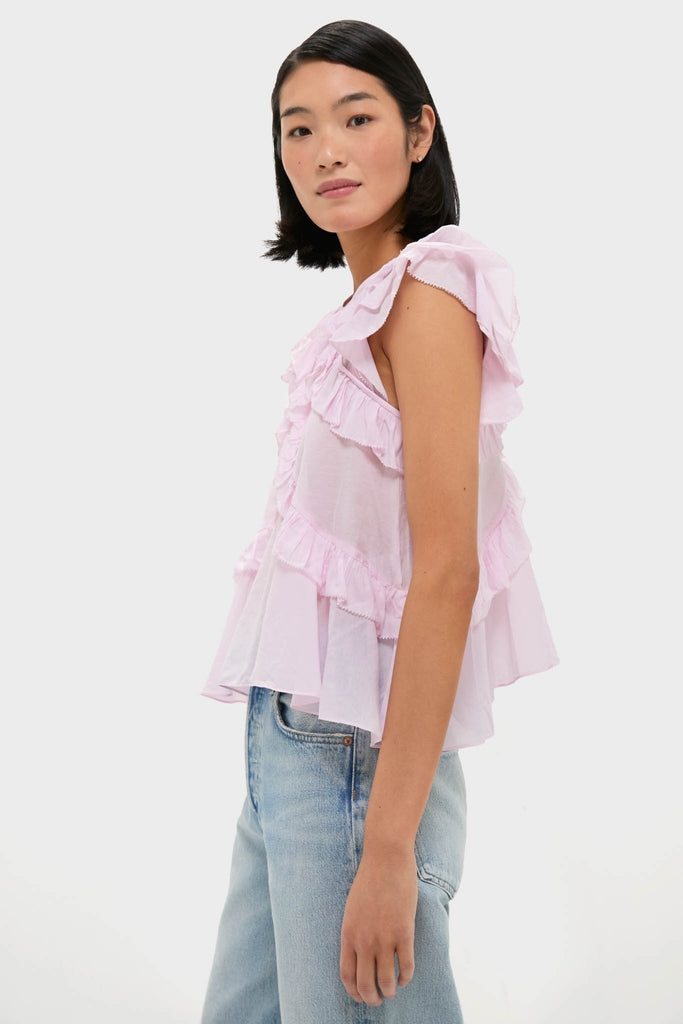 Young woman in profile wearing the classic Light Pink Nalou Top, showcasing effortless ruffles and flutter sleeves, paired with light-wash jeans for a fun, high-end look.