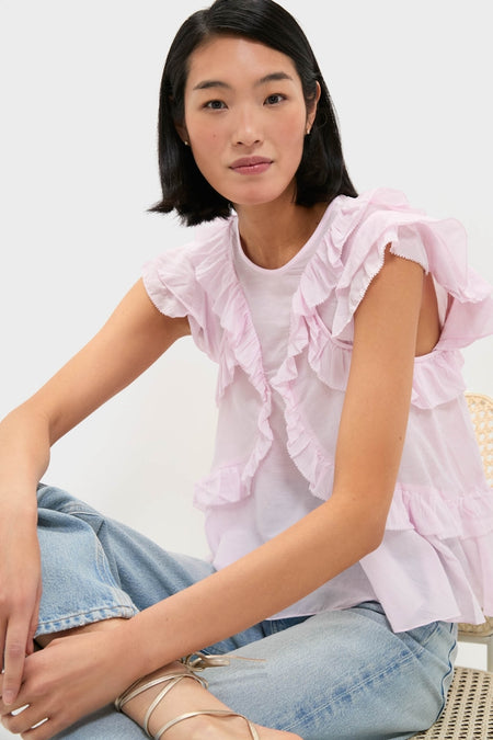 Woman in light-wash jeans and classic Light Pink Nalou Top with ruffle accents and flutter sleeves, seated casually on a chair, embodying an effortless and high-end style.