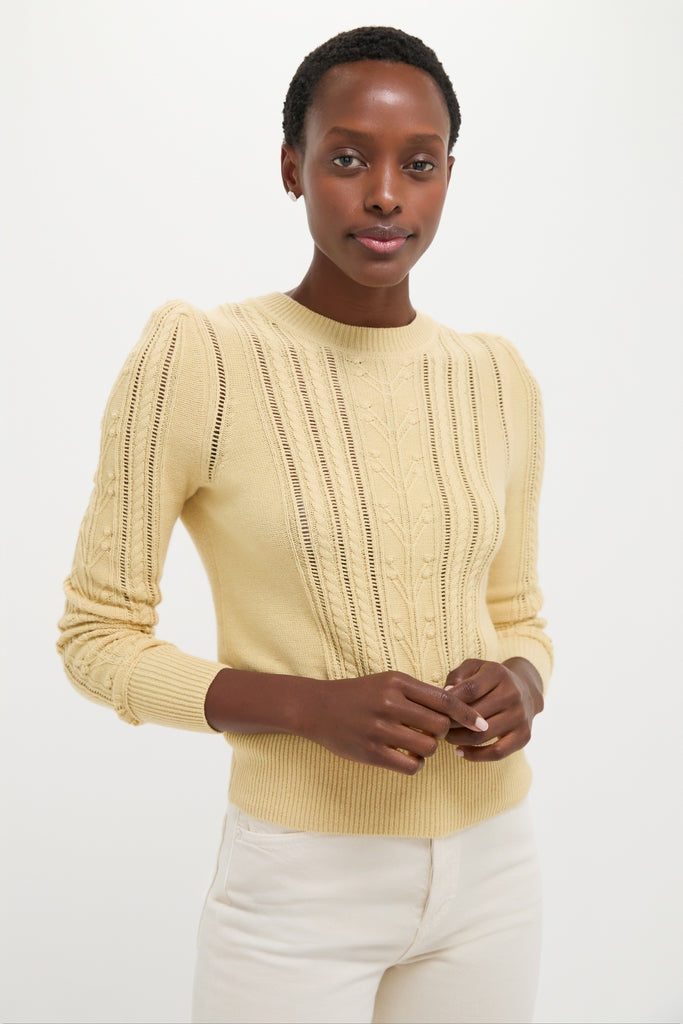 Young woman in a classic, light yellow Kalyn Sweater with cable knit detailing, exuding an effortless, high-end style, paired with cream pants for a fun, chic look.