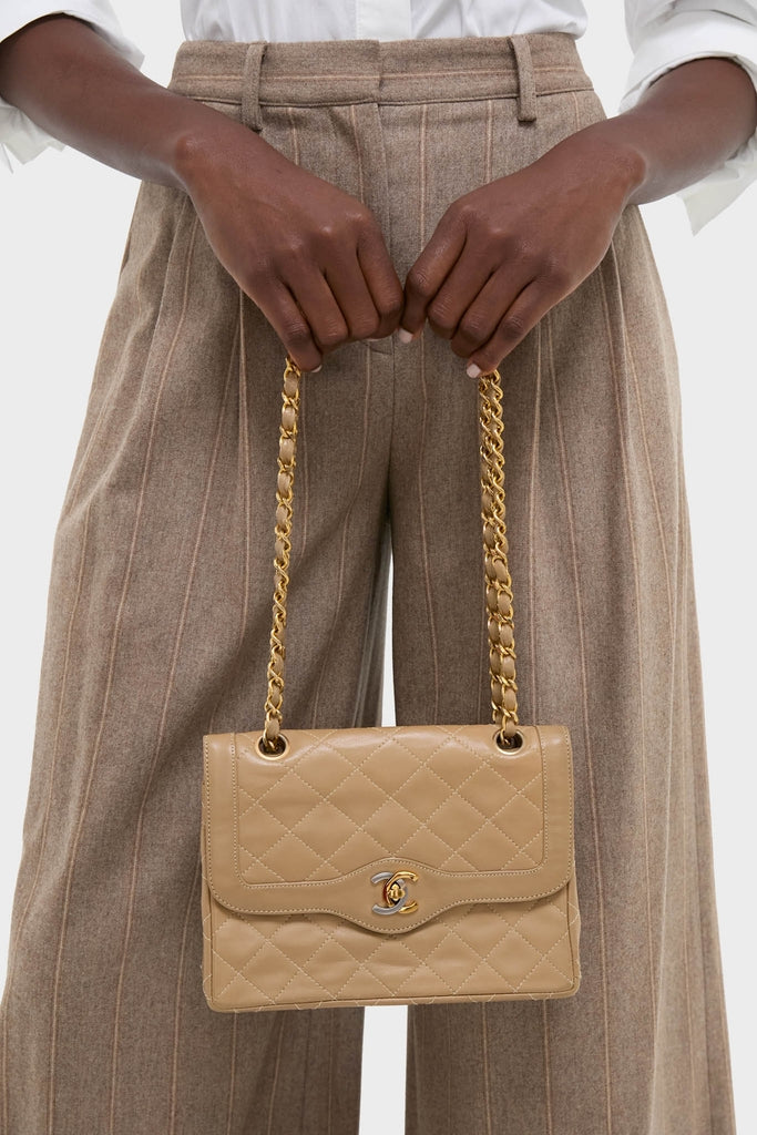 CHANEL CC Mini Paris Double Flap Bag, a classic quilted leather shoulder bag with gold chain and logo clasp, held effortlessly by someone in stylish pinstriped trousers.