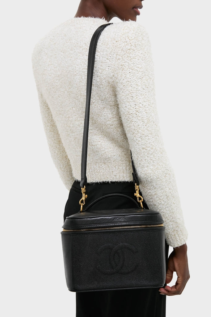 Woman in white top carries a classic CHANEL Large Caviar Vanity Bag. The black leather bag features gold-tone hardware, exuding an effortless, high-end style.